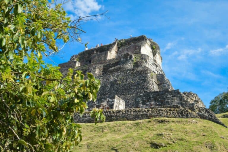 A scenic view of a stone pyramid ruins atop a grassy hill under a blue sky.