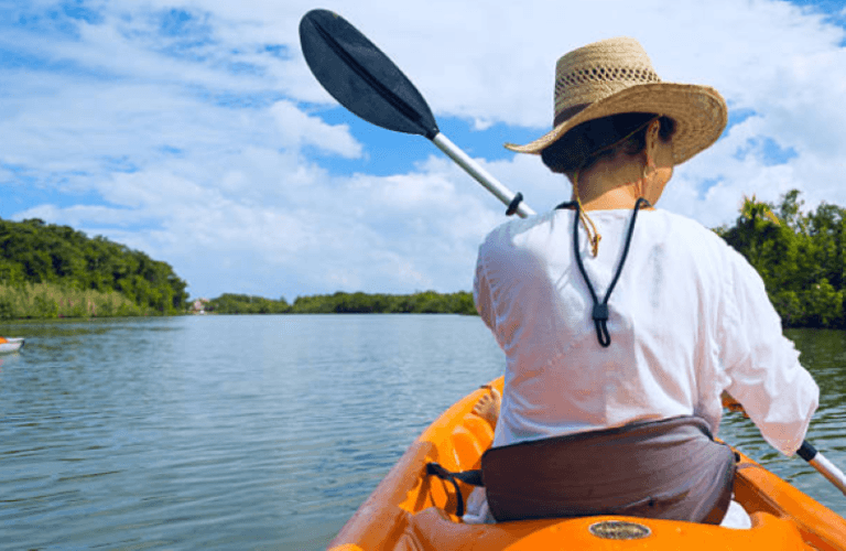 A person kayaking on a calm river under a blue sky with scattered clouds.