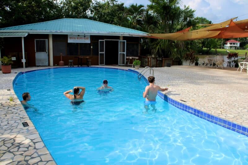 Four people enjoying a swim in a blue pool surrounded by greenery and a nearby building.