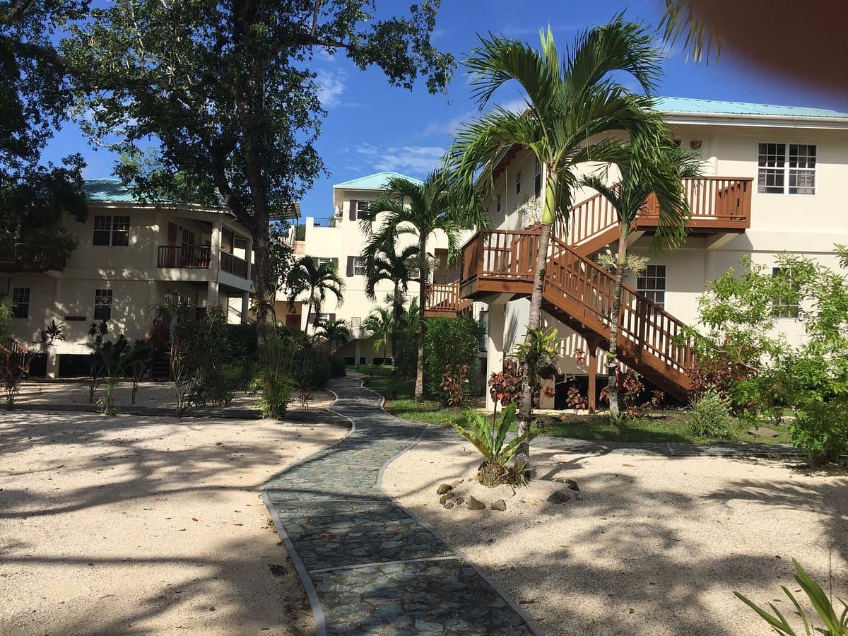 A pathway winds through a tropical garden leading to multi-level buildings with balconies.