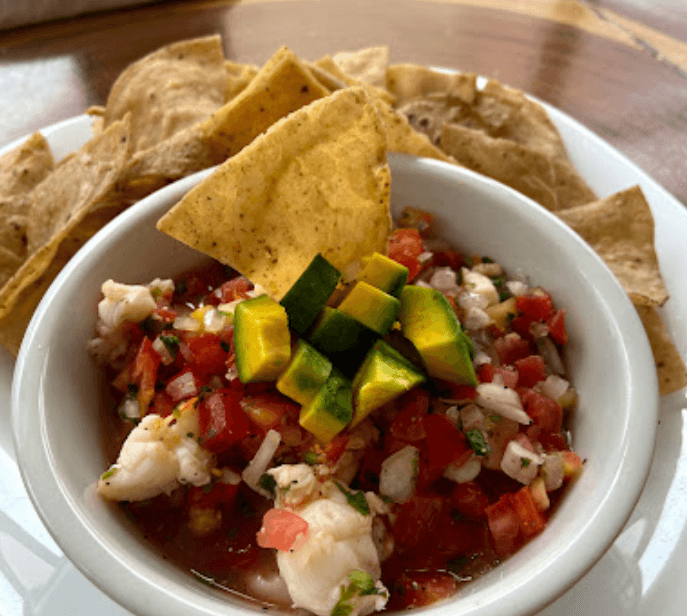 A bowl of shrimp ceviche topped with diced avocado and tortilla chips.