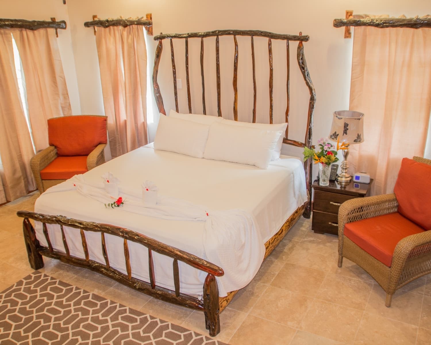 A cozy bedroom featuring a wooden bed frame, two orange chairs, and natural light from nearby curtains.