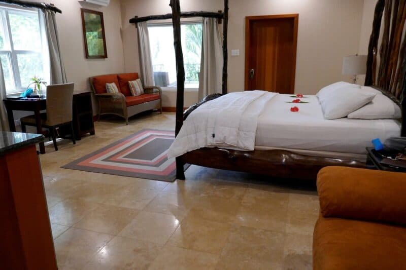A cozy hotel room featuring a bed, seating area, and a desk with natural light coming through the windows.