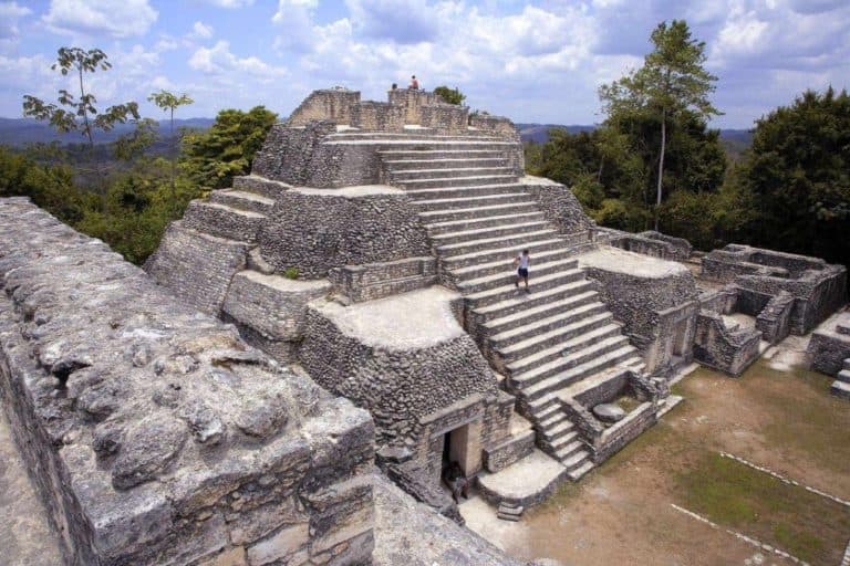 Ancient stone pyramid structure surrounded by greenery under a blue sky.