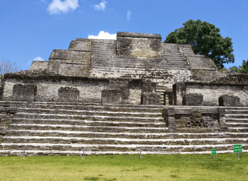 Ancient stone temple with steep steps and a grassy foreground under a blue sky.