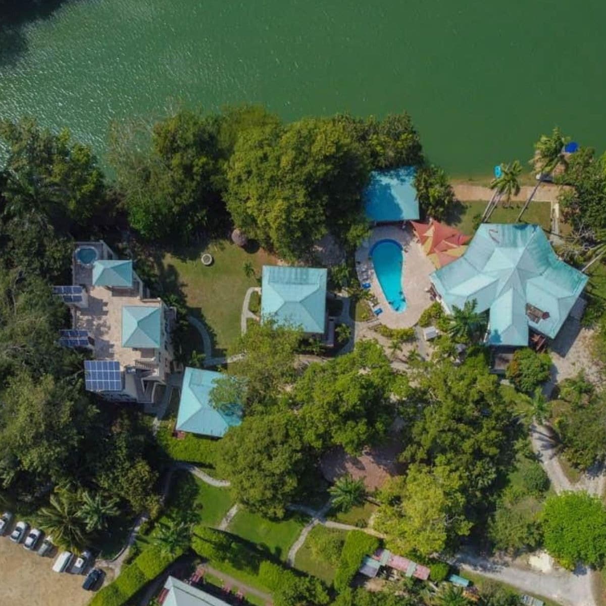 Aerial view of a tropical property featuring several buildings, a swimming pool, and lush greenery by the water.