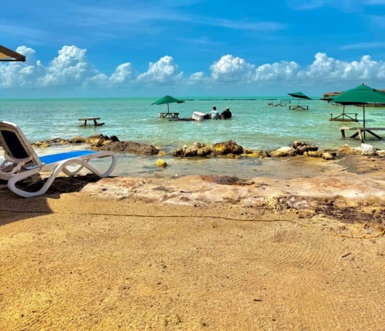 A serene beach scene with turquoise water, green umbrellas, and distant cloud formations.