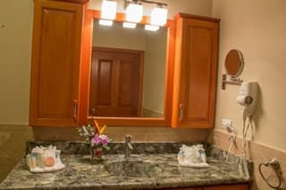 A well-lit bathroom with a granite countertop, wooden cabinets, a mirror, and toiletries arranged neatly.