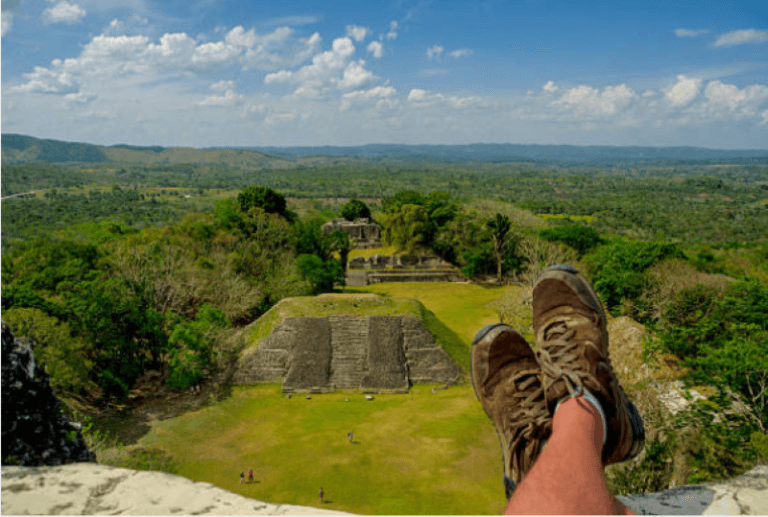 A person relaxes while looking down at ancient ruins surrounded by lush green landscape.