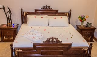 A beautifully arranged bed with rose petals and decorative towels in a cozy bedroom setting.