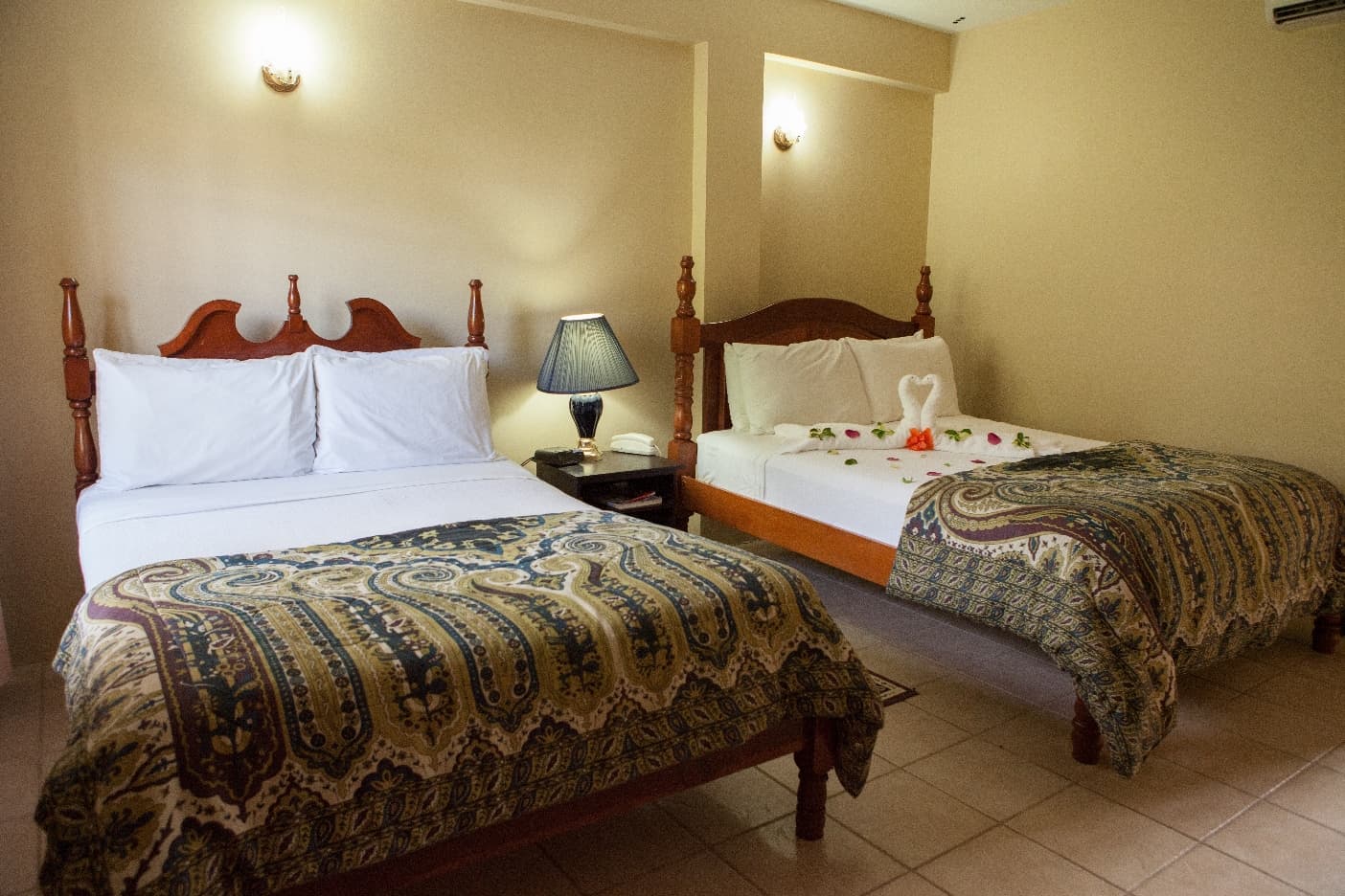 A cozy hotel room featuring two beds, a bedside lamp, and decorative flowers on one bed.