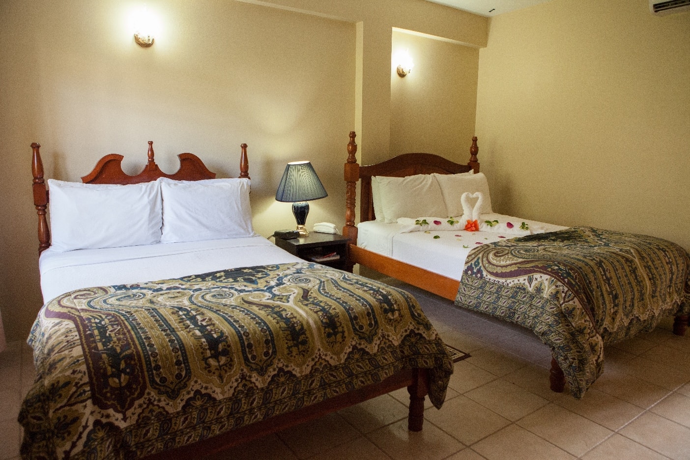 A cozy hotel room featuring two beds, a bedside lamp, and decorative flowers on one bed.