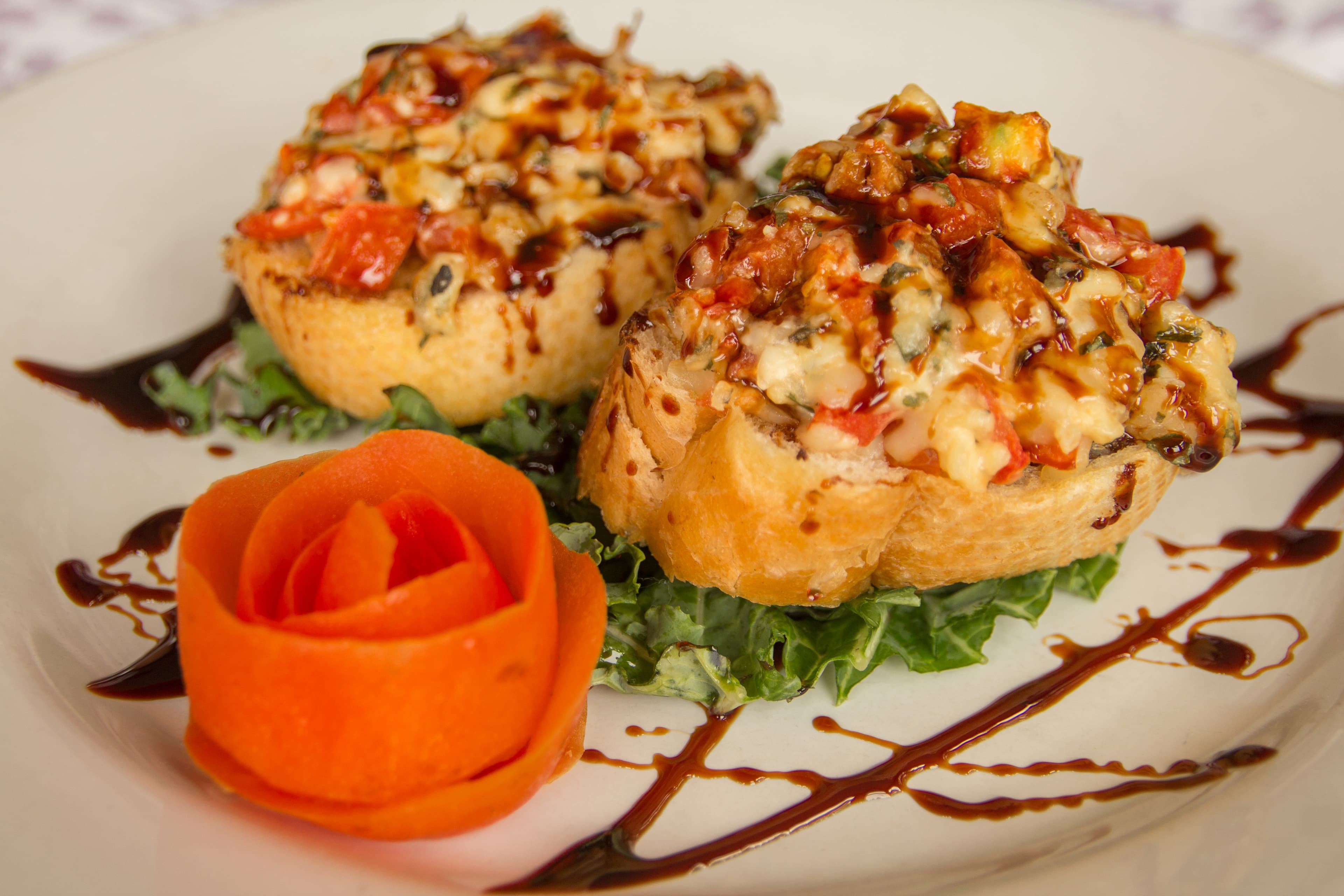 Two stuffed bread halves garnished with a rose made of carrot on a bed of lettuce, drizzled with sauce.