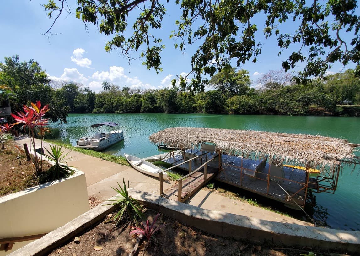 A serene river scene featuring a boat docked near a thatched-roof platform surrounded by lush greenery.