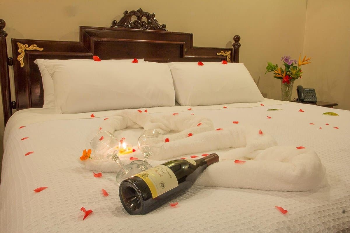 A romantic hotel room featuring a bed adorned with rose petals, champagne, and soft towels.