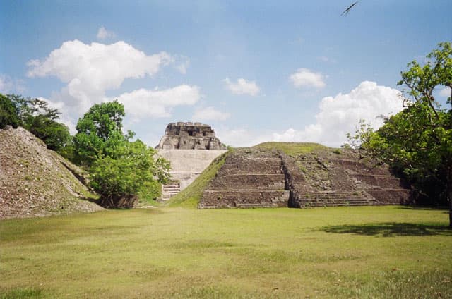 A grassy area with ancient pyramid structures under a blue sky with scattered clouds.