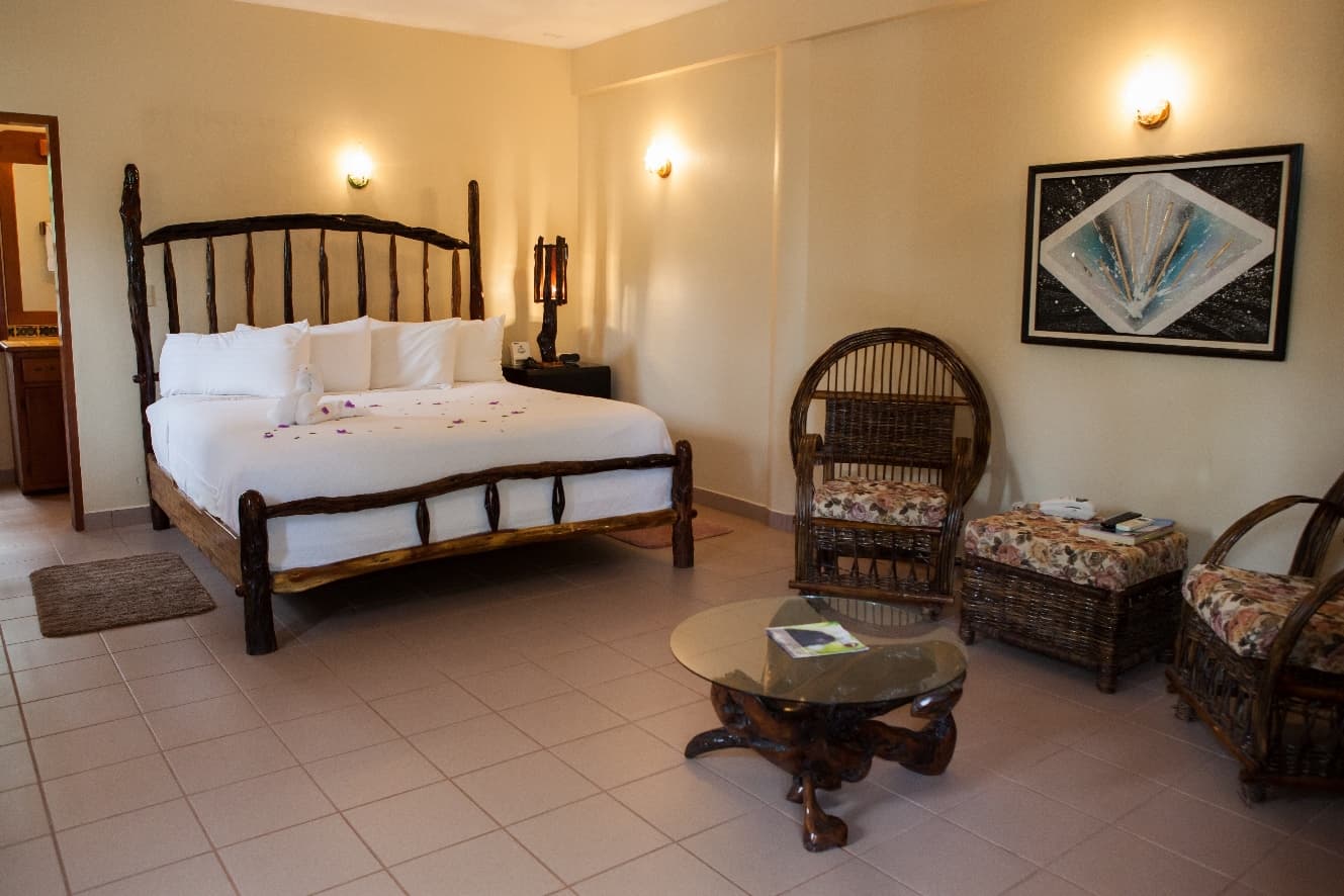 A cozy hotel room featuring a wooden bed, wicker chairs, and soft lighting.