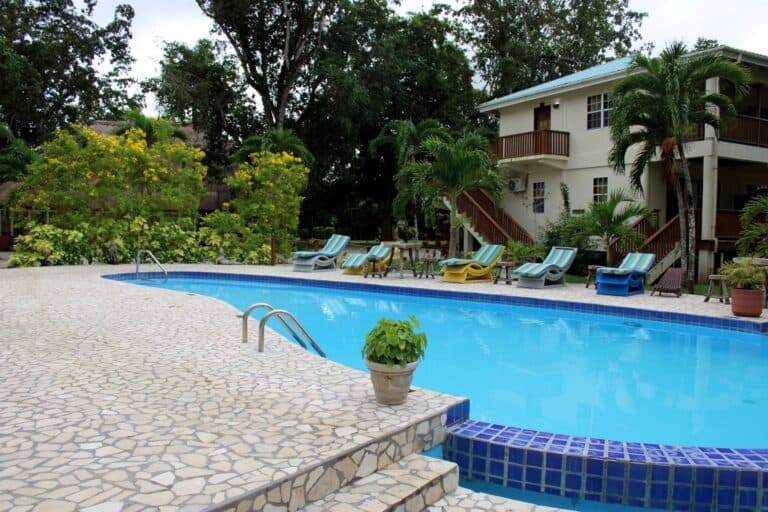 A tranquil pool area surrounded by greenery and lounge chairs beside a building.