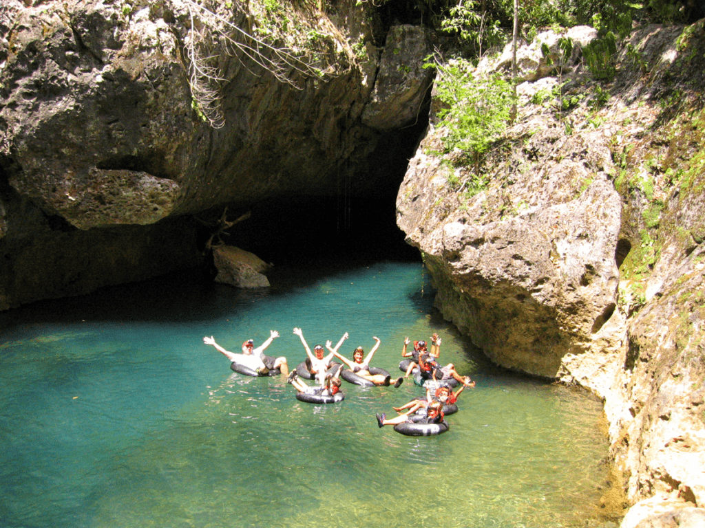 A group of people joyfully floating on inner tubes in a clear blue lagoon surrounded by rocky cliffs.