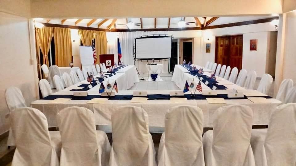 A conference room set up with long tables, white chairs, and flags arranged for a meeting.