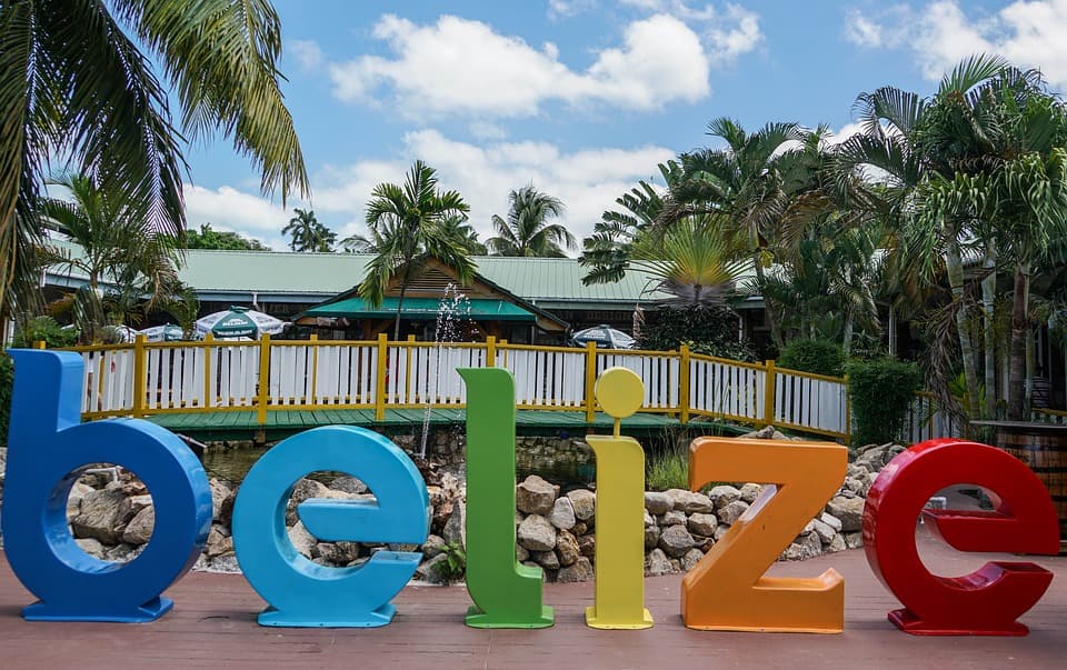 Colorful "Belize" sign with palm trees and a building in the background.