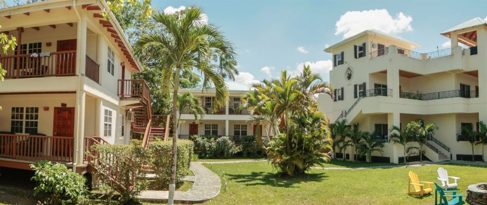 A panoramic view of a courtyard surrounded by tropical plants and two-story buildings.