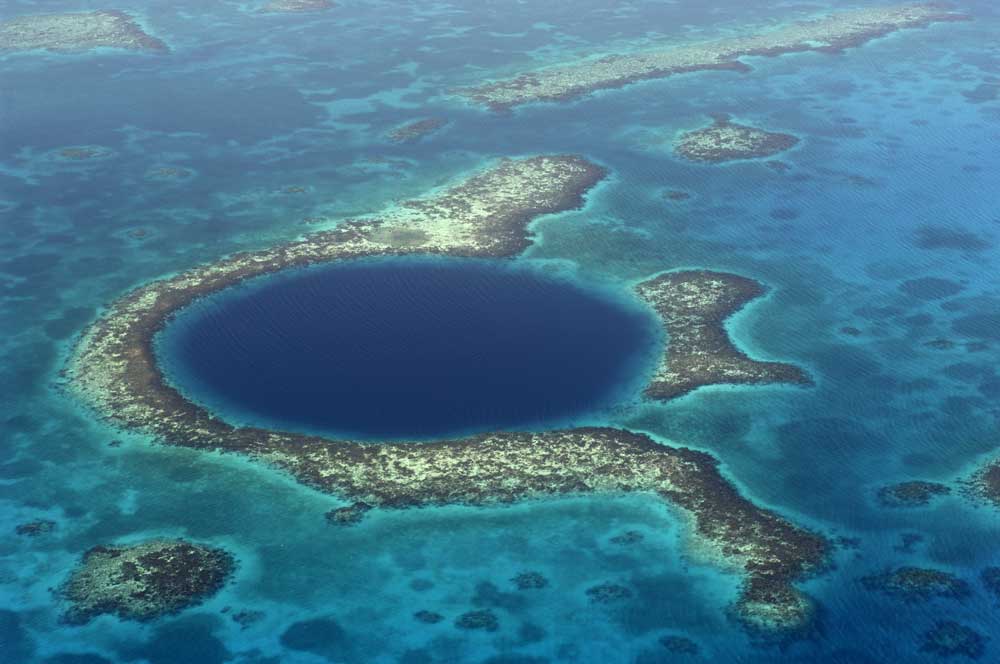 Aerial view of the Blue Hole surrounded by coral reefs in turquoise waters.