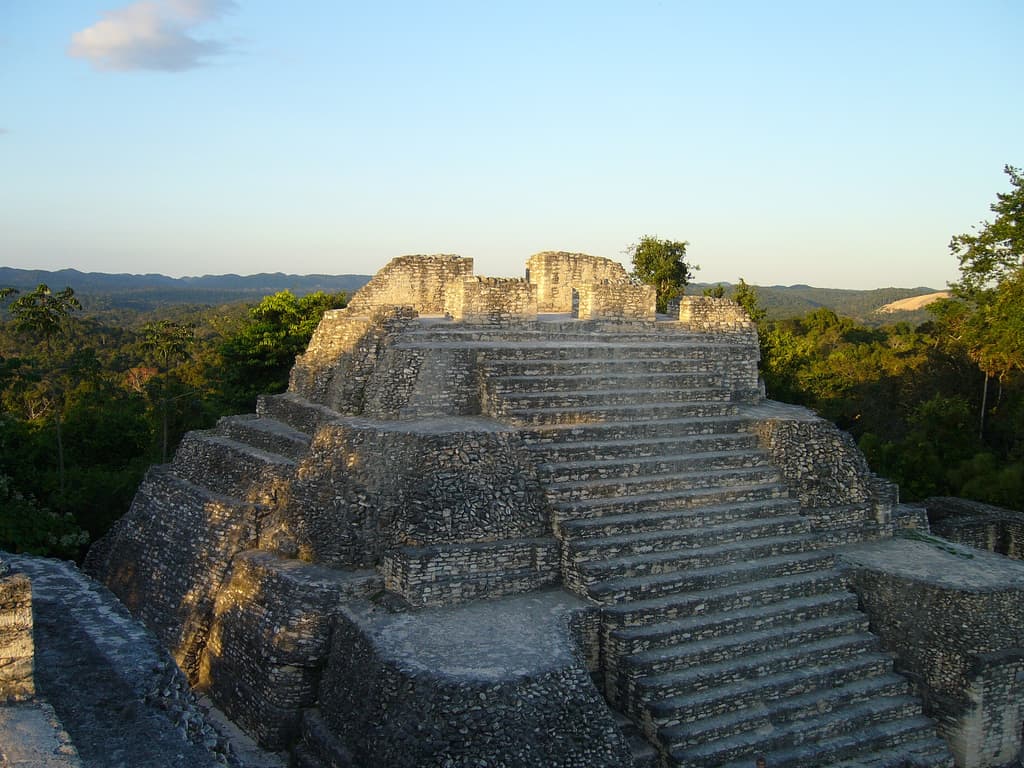 Ancient stone pyramid amidst lush greenery under a clear sky.