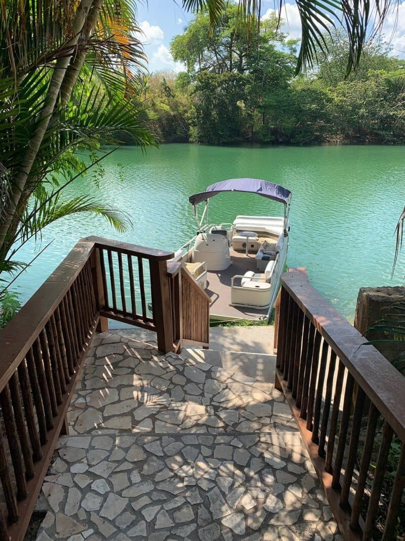 A wooden stairway leads down to a green lake with a boat docked at the shore.