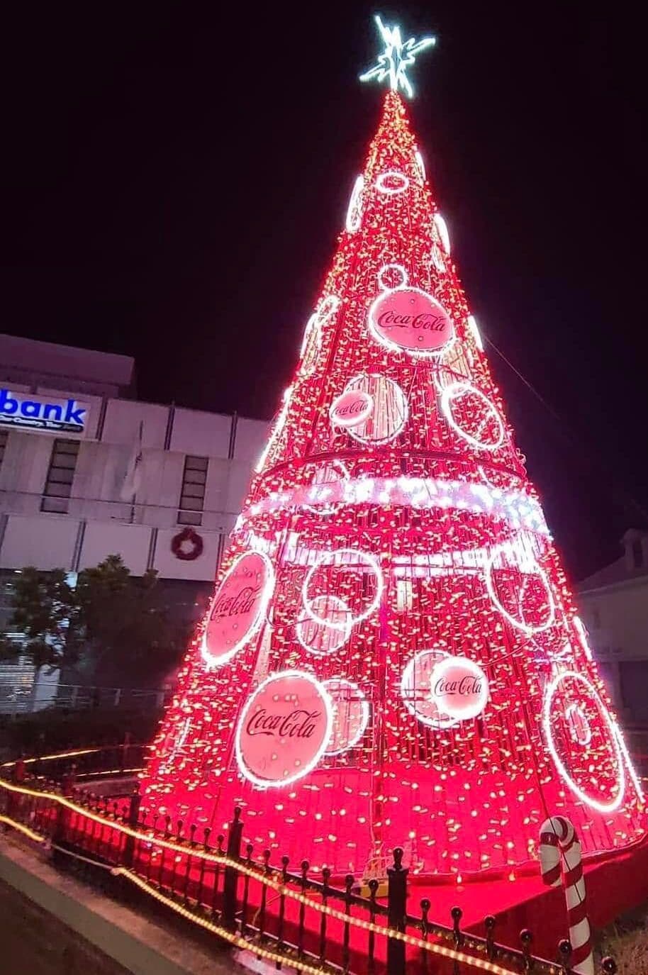 A brightly lit Christmas tree adorned with Coca-Cola logos at night.