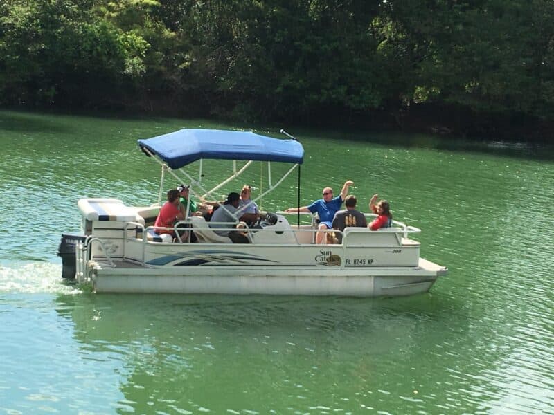 A group of people enjoying a day on a pontoon boat in a green lake.